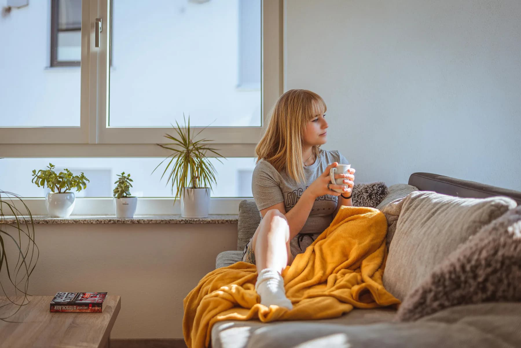 Kvinne med en kopp kaffe i sofaen ved vinduet, ettertenksom over økonomien